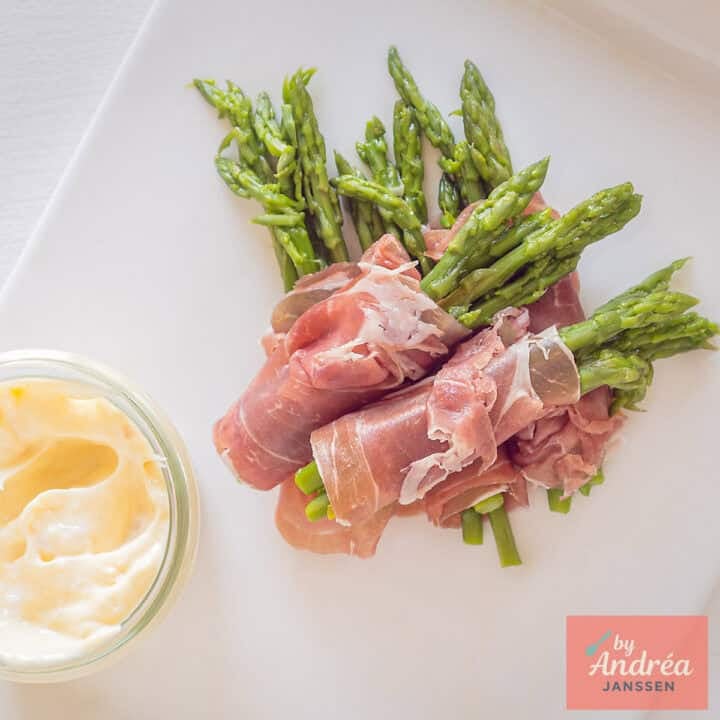 A square picture taken from above with a white plate with homemade aioli and green asparagus in parma ham appetizers