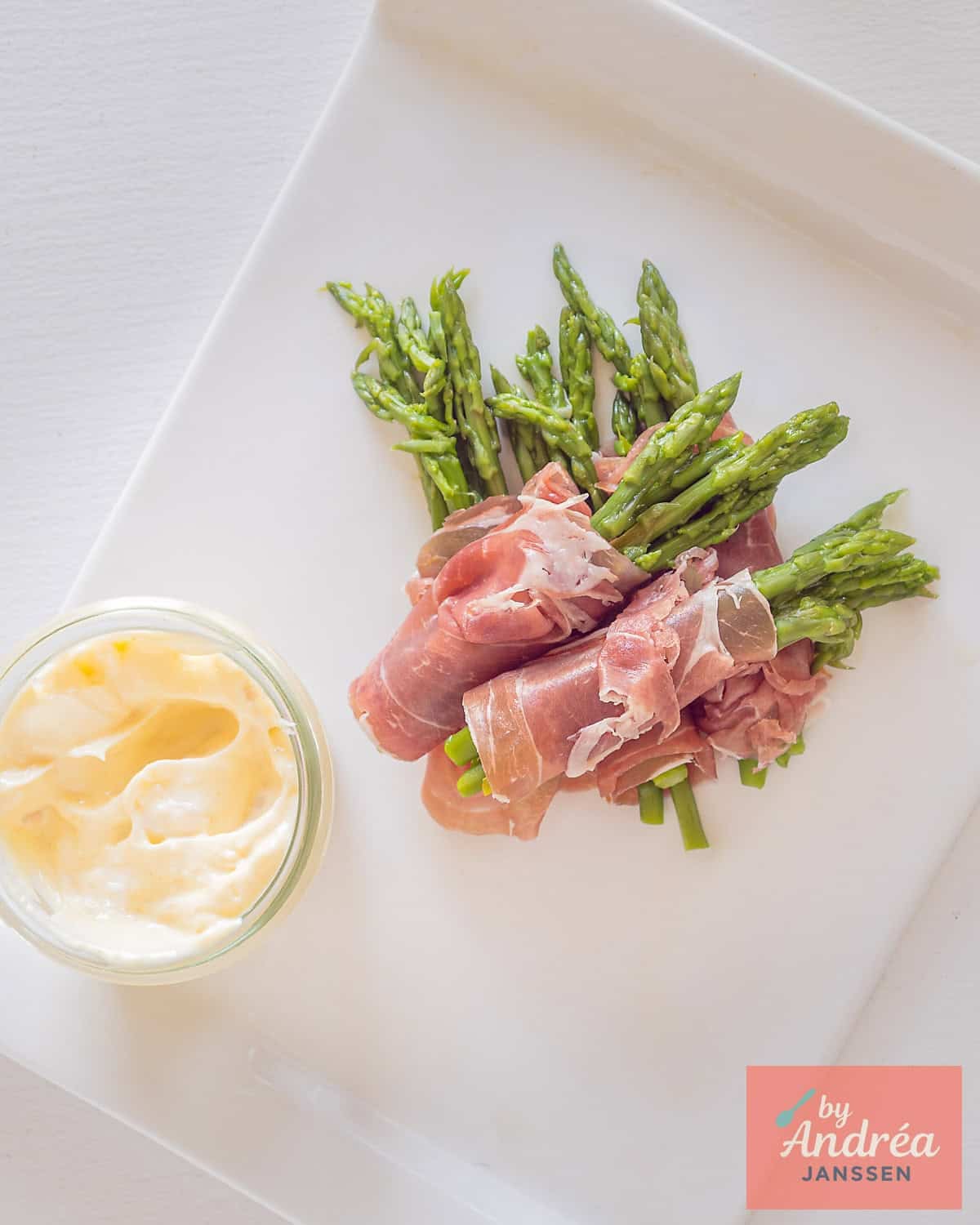 A picture taken from above a white plate with green asparagus wrapped in parma ham and aioli made from scratch