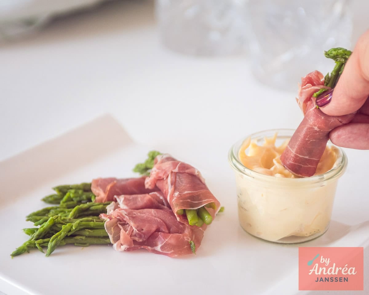 A width picture with some green asparagus with parma ham appetizers, one is dipped in a jar with homemade aioli