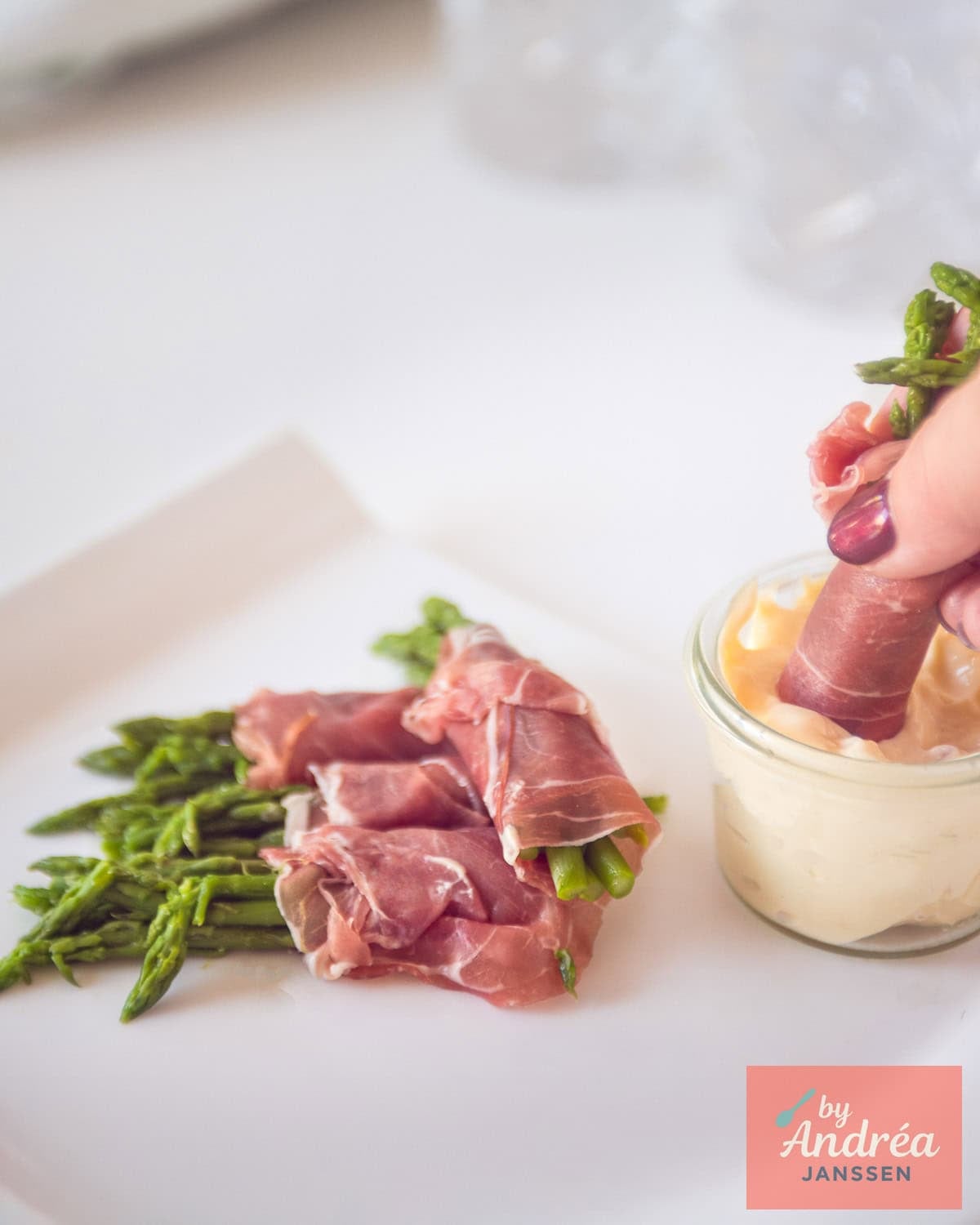 Some green asparagus appetizers on a white plate an appetizer dipping in a homemade aioli dip.