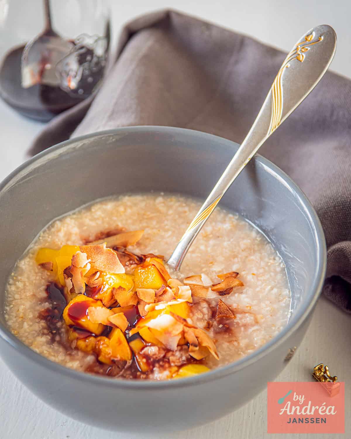 A pink bowl with oatmeal, date syrup, mango, and coconut on a white background.