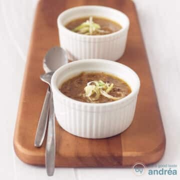 A square photo with two bowls filled with leek soup with cabbage. Two spoons next to it on a wooden board. A white background.