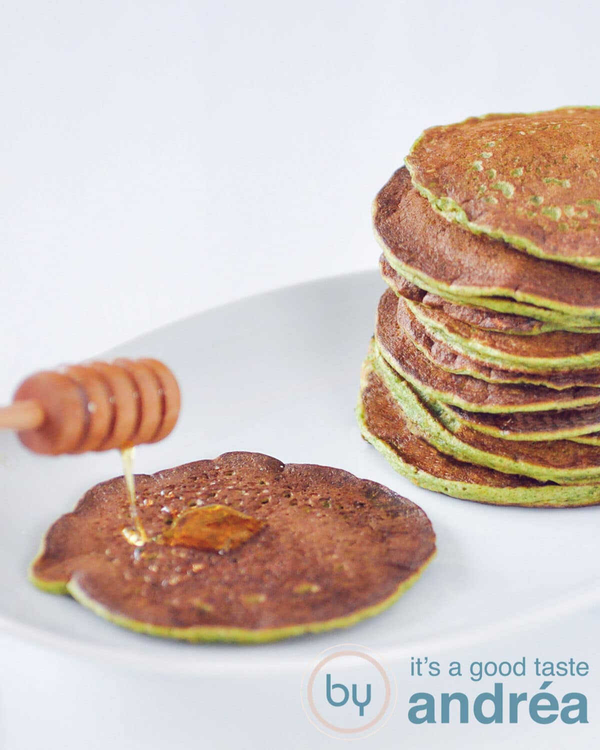 a white plate with spinach pancakes. One got some honey drizzled on top
