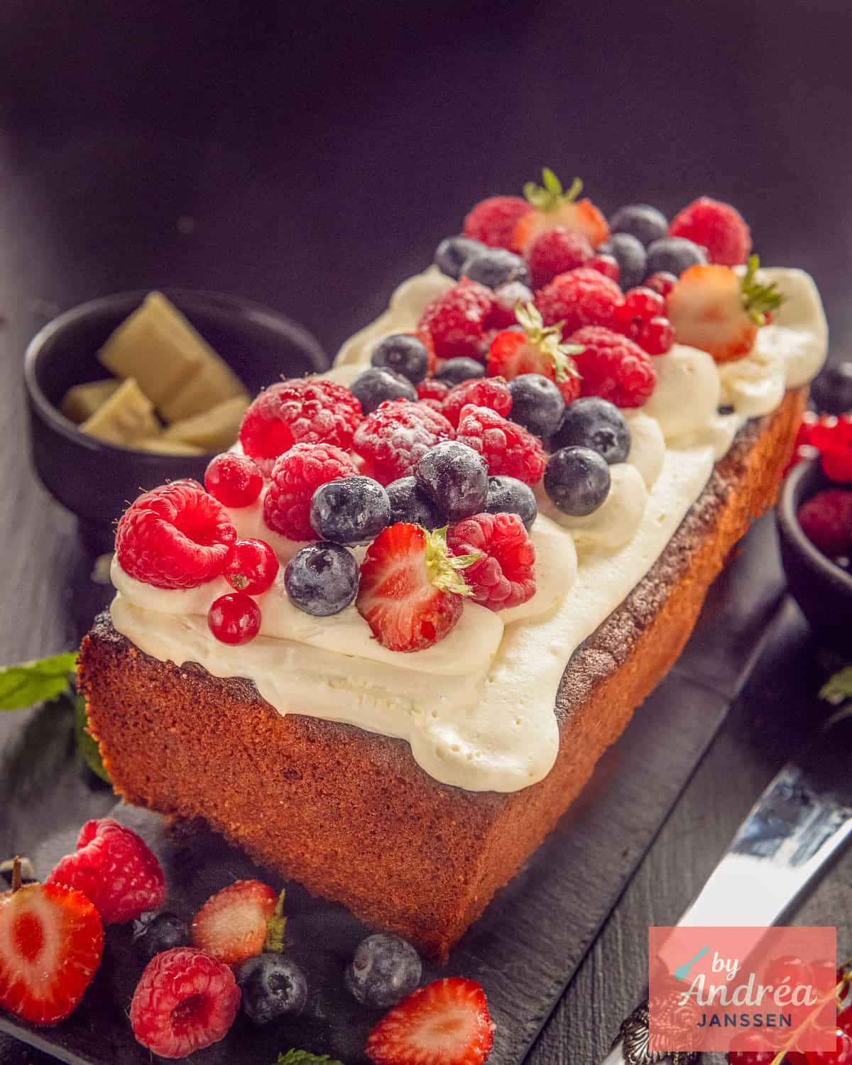 A white chocolate cake on a black base with buttercream and fresh fruit.