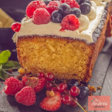 A square photo with a white chocolate cake, buttercream, and fresh red fruit on a dark background.