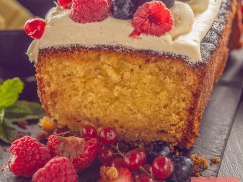 A square photo with a white chocolate cake, buttercream, and fresh red fruit on a dark background.