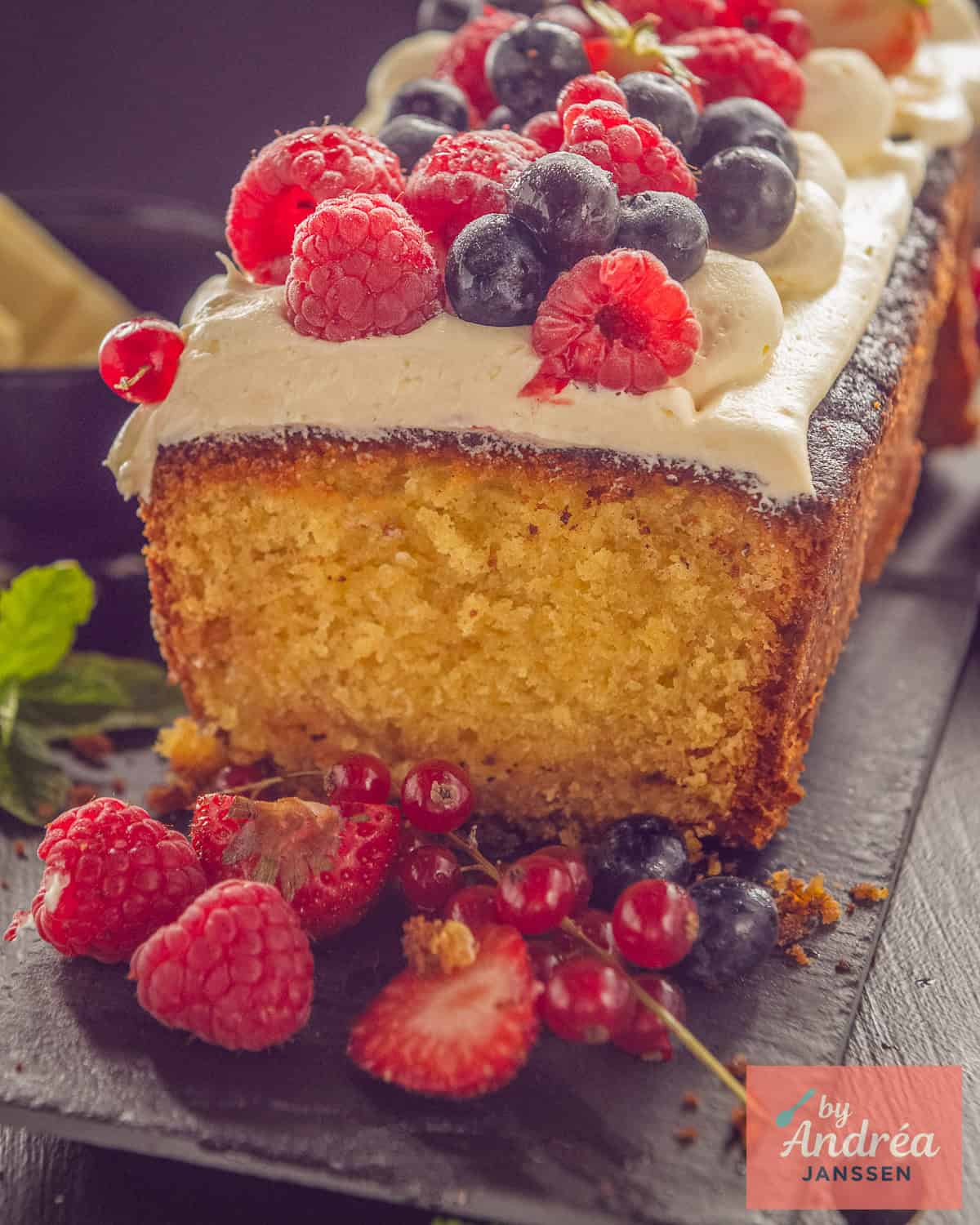 A white chocolate cake with a slice cut off revealing the inside. Fresh fruit and buttercream on top.