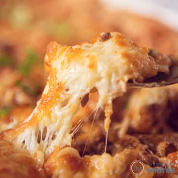 A square photo of a spoon with a scoop of shepherd's pie filling, in the background the rest of the baking dish.
