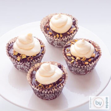 A square picture with a cakestand, white, with four chocolate cupcakes including ganache and topping