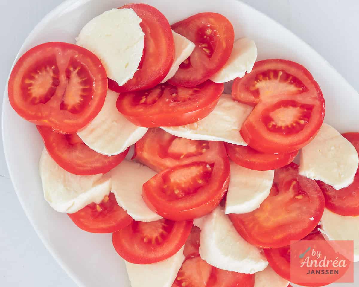 Slices of tomato and mozzarella lie alternately on a white plate.