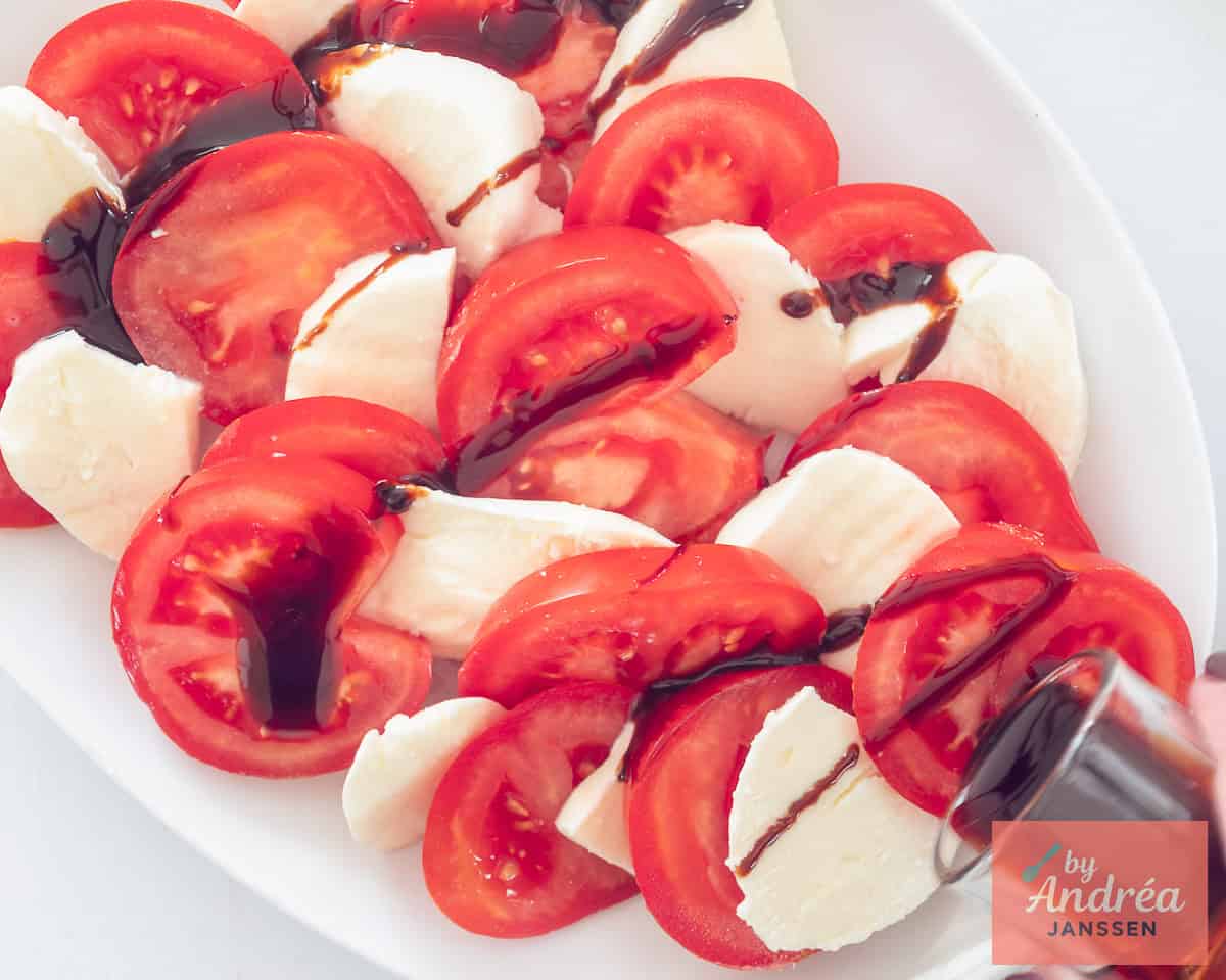 Slices of tomato and mozzarella alternate on a plate with a drizzle of balsamic vinegar.