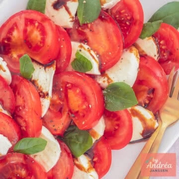 A square photo of sliced ​​tomatoes, basil, mozzarella and balsamic vinegar on a white plate.