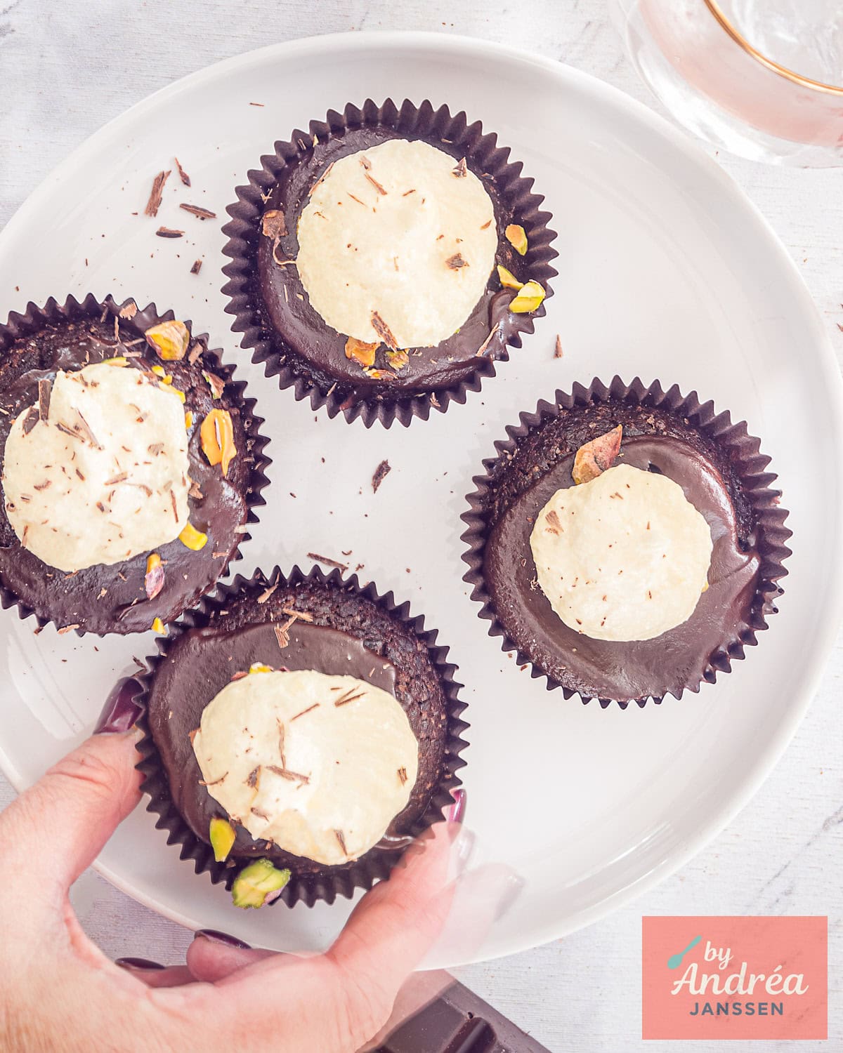 Een foto van bovenaf van vier chocolade cupcakes met ganache, witte chocolade botercrème en pistache
