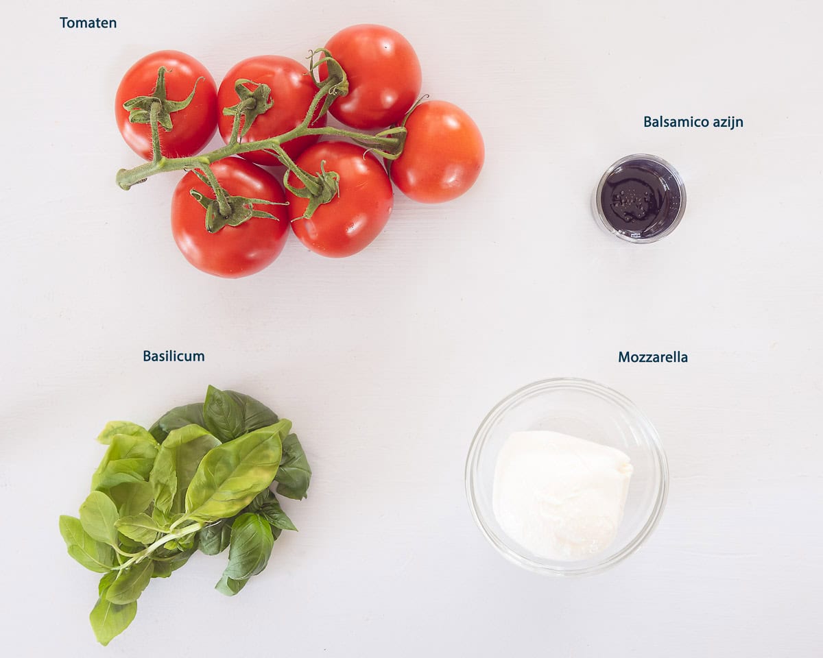 Ingredienten Caprese Salade Met Mozzarella En Tomaat op een witte ondergrond met tekstbeschrijving.