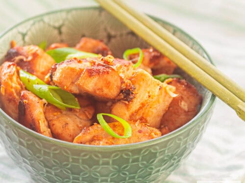 A square photo of a green bowl containing a dish of chicken seasoned with four sauces, inspired by Thai cuisine.