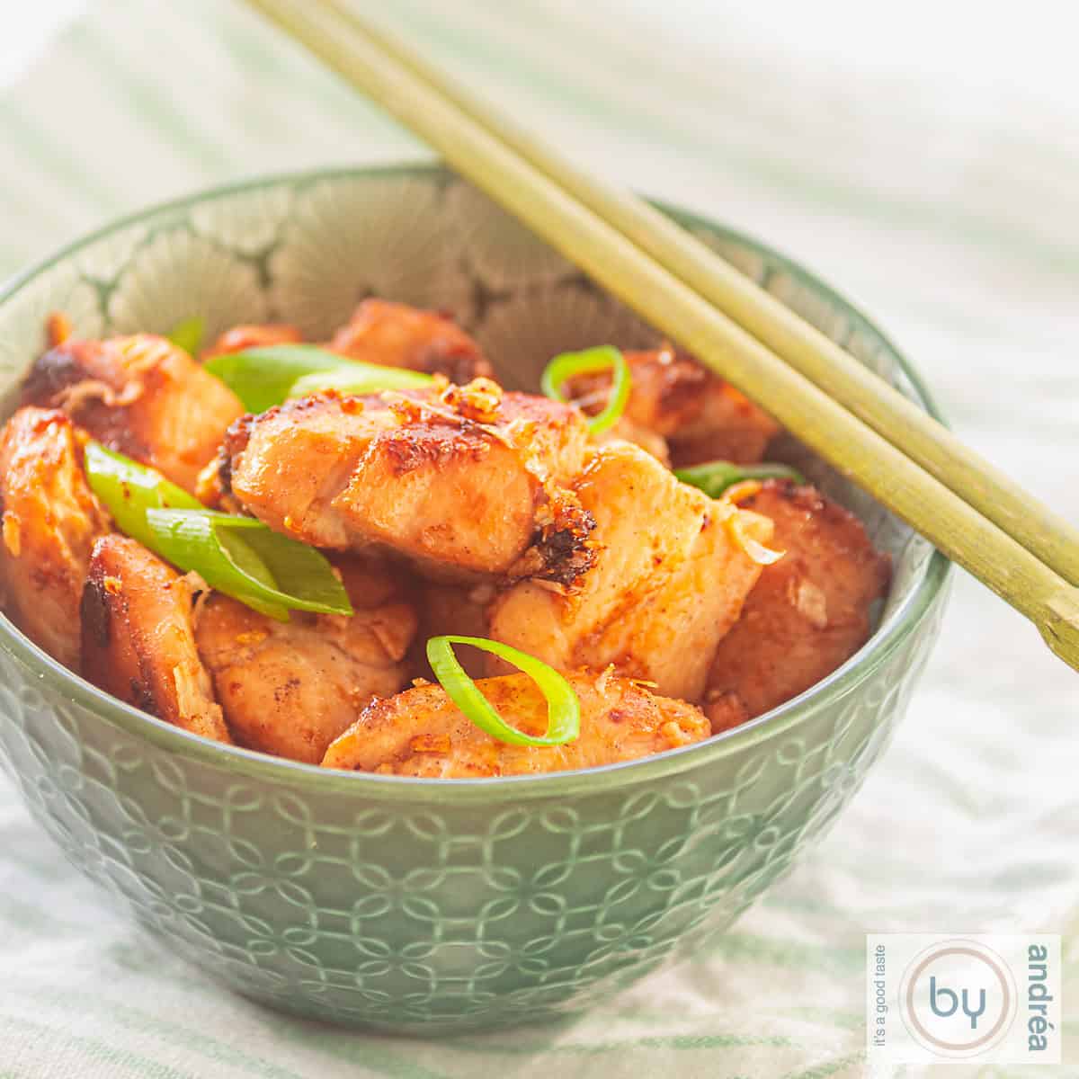 A square photo of a green bowl containing a dish of chicken seasoned with four sauces, inspired by Thai cuisine.