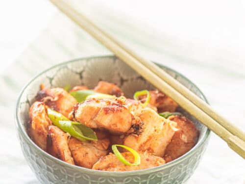 A green bowl of chicken with 4 flavors seasoned. Two chopsticks are on top of it. The bowl is on a green white striped towel