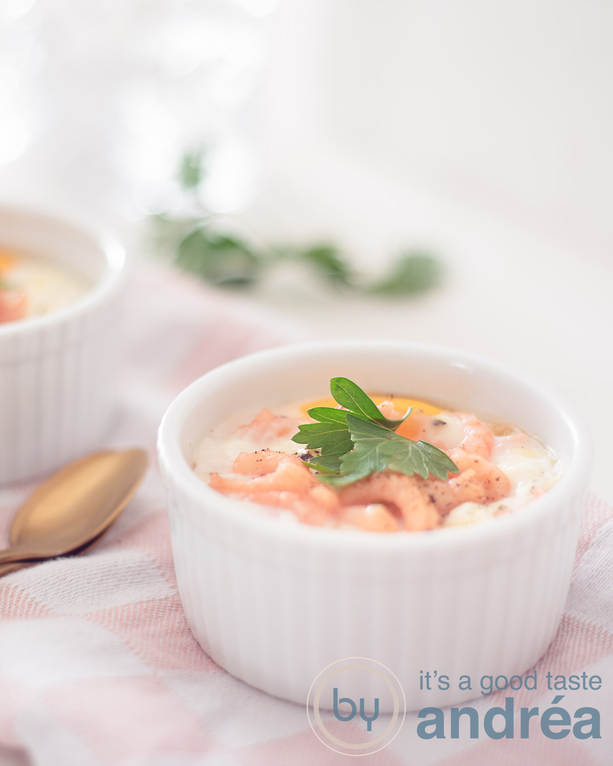 A white bowl filled with egg and shrimp prepared in the steam oven. Garnish of parsley on a white pink cloth. A white underground.