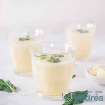 A square photo with three glasses filled with a vanilla, pear and coconut water smoothie. With fresh mint, which is also around it. A white background