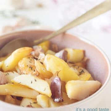a pink bowl, roast potatoes with cloves of garlic and thyme spread on top