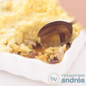 A square photo with part of a white casserole filled with mackerel, zucchini and mashed potatoes