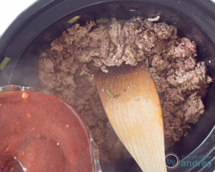 A slow cooker with ground beef, on which the sloppy joe sauce is poured