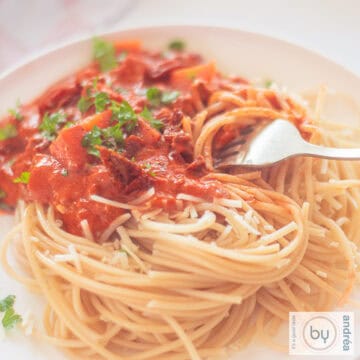 A square photo with a plate of spaghetti with sauce containing mascarpone, ground beef and tomato.