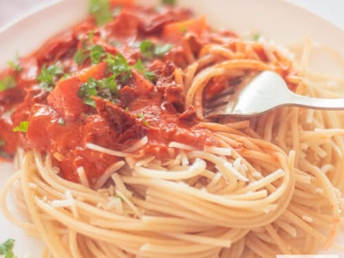 A square photo with a plate of spaghetti with sauce containing mascarpone, ground beef and tomato.