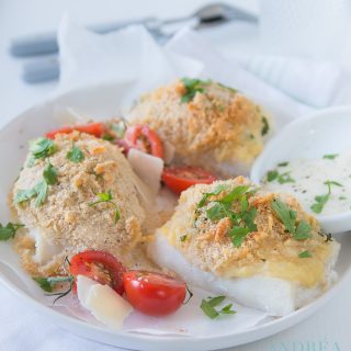 3 cod filets grained with cheese bread crust on a white plate with some veggies.