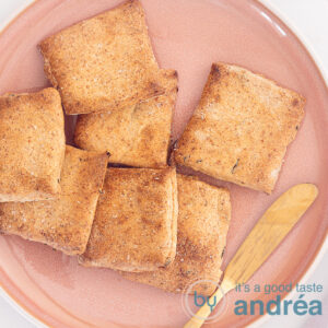 A pink plate on a white background filled with whole grain crackers with herbs