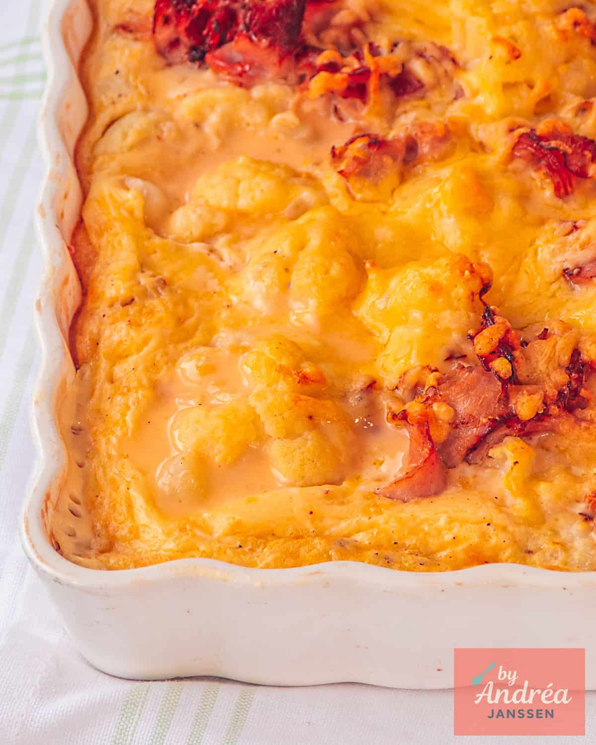 Een deel van een ovenschaal gevuld met bloemkool, spekjes, roomsaus en kaas.