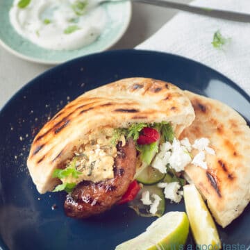 A blue plate with grilled vegetables, hamburger and feta cheese.
