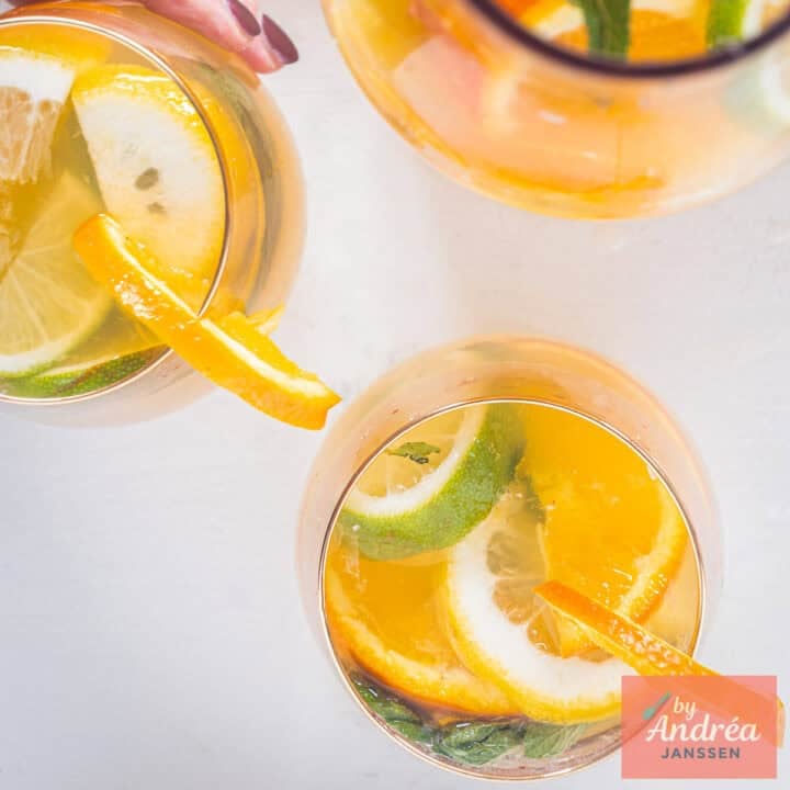 A square picture: Homemade orange iced tea with lemon and lime wedges, mint and ice cubes in a glass