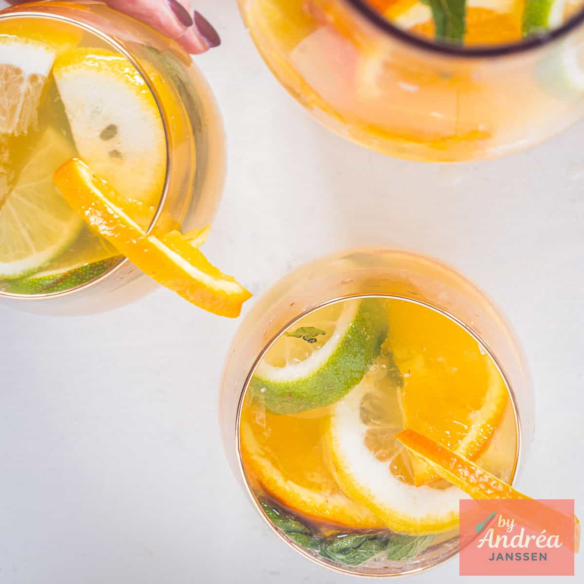 A square picture: Homemade orange iced tea with lemon and lime wedges, mint and ice cubes in a glass