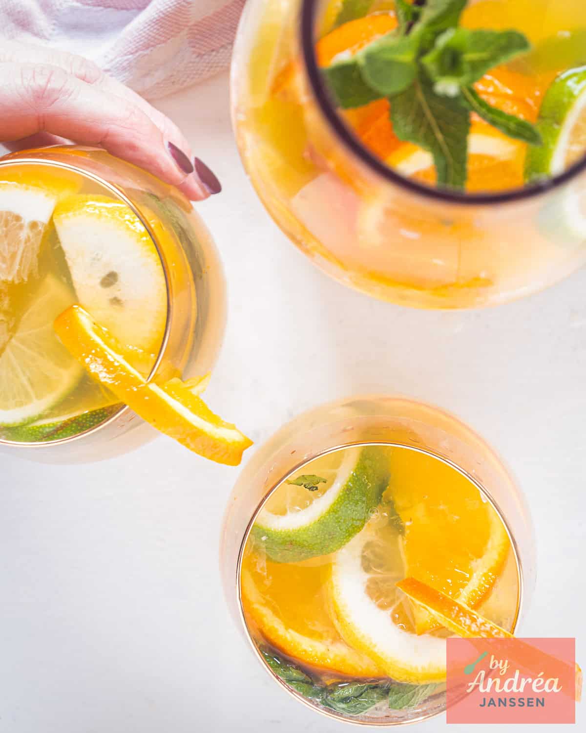 Homemade orange iced tea with lemon and lime wedges, mint and ice cubes in a glass