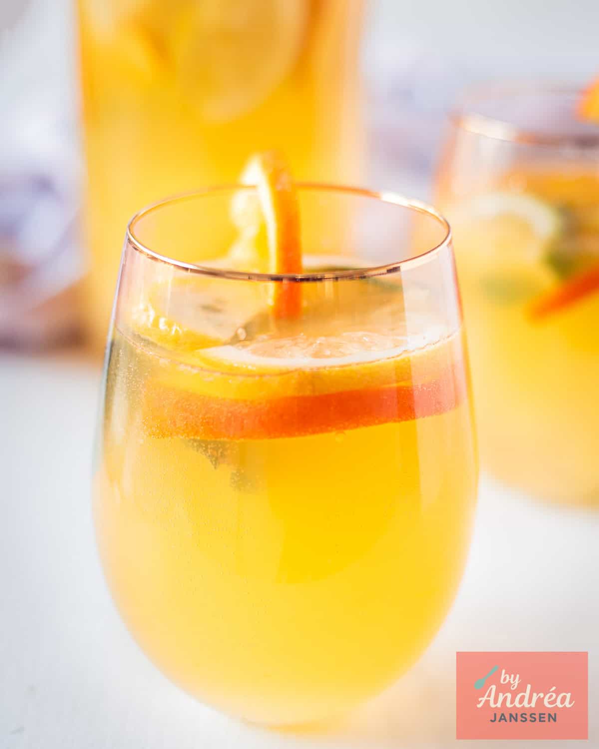 Orange iced tea in a large jar with citrus slices, mint sprigs and big ice cubes
