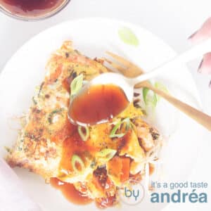 A square picture of a white plate with Egg Foo Young, some sauce dripping onto it.