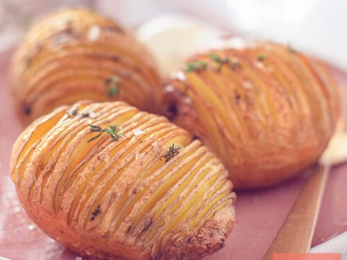 A square photo of three hasselback potatoes and crème fraîche on a pink plate.