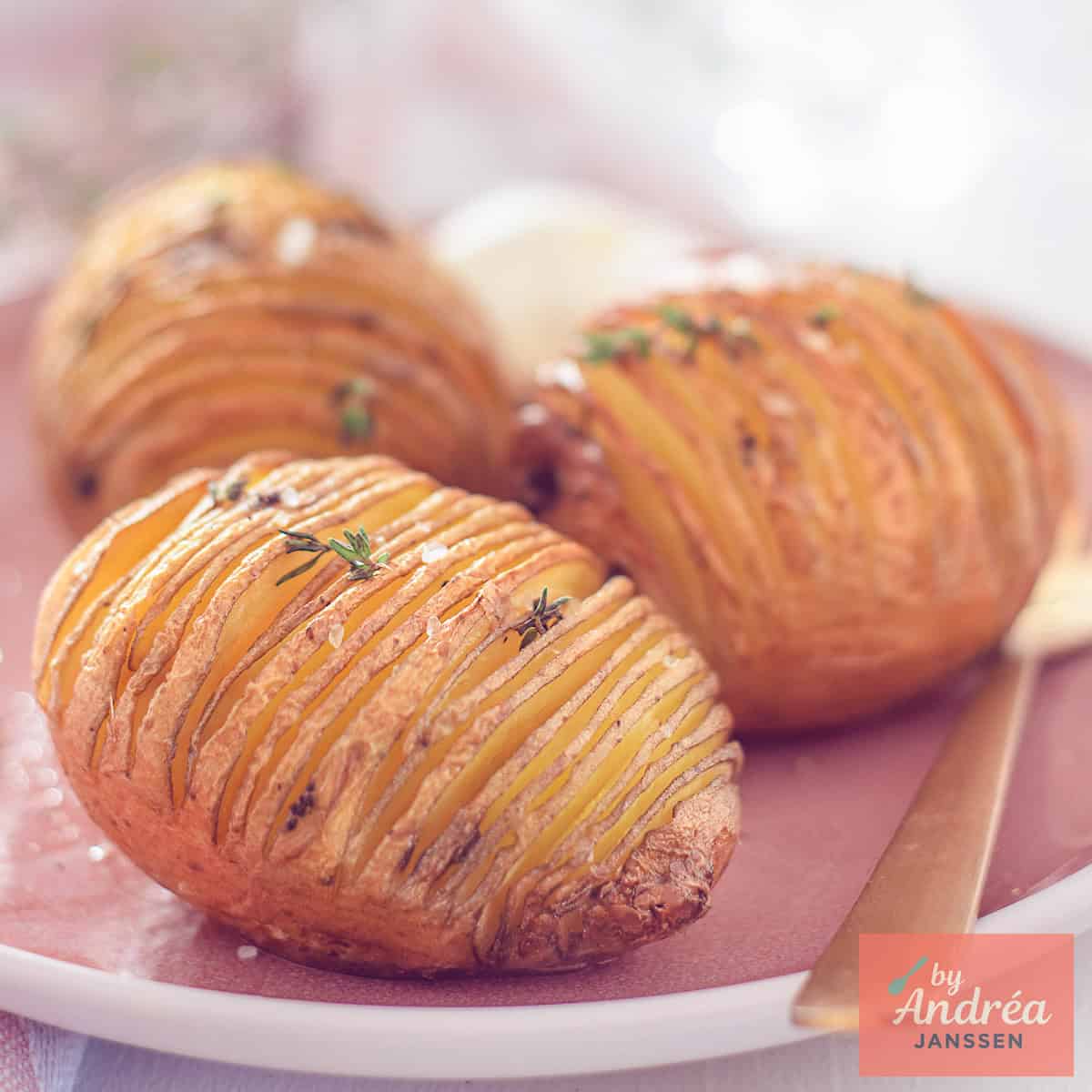 A square photo of three hasselback potatoes and crème fraîche on a pink plate.