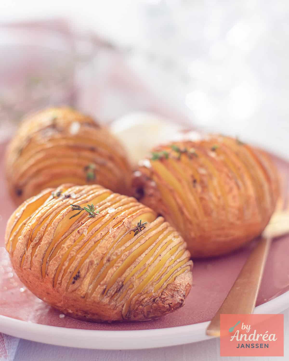 Three hasselback potatoes on a pink plate with thyme
