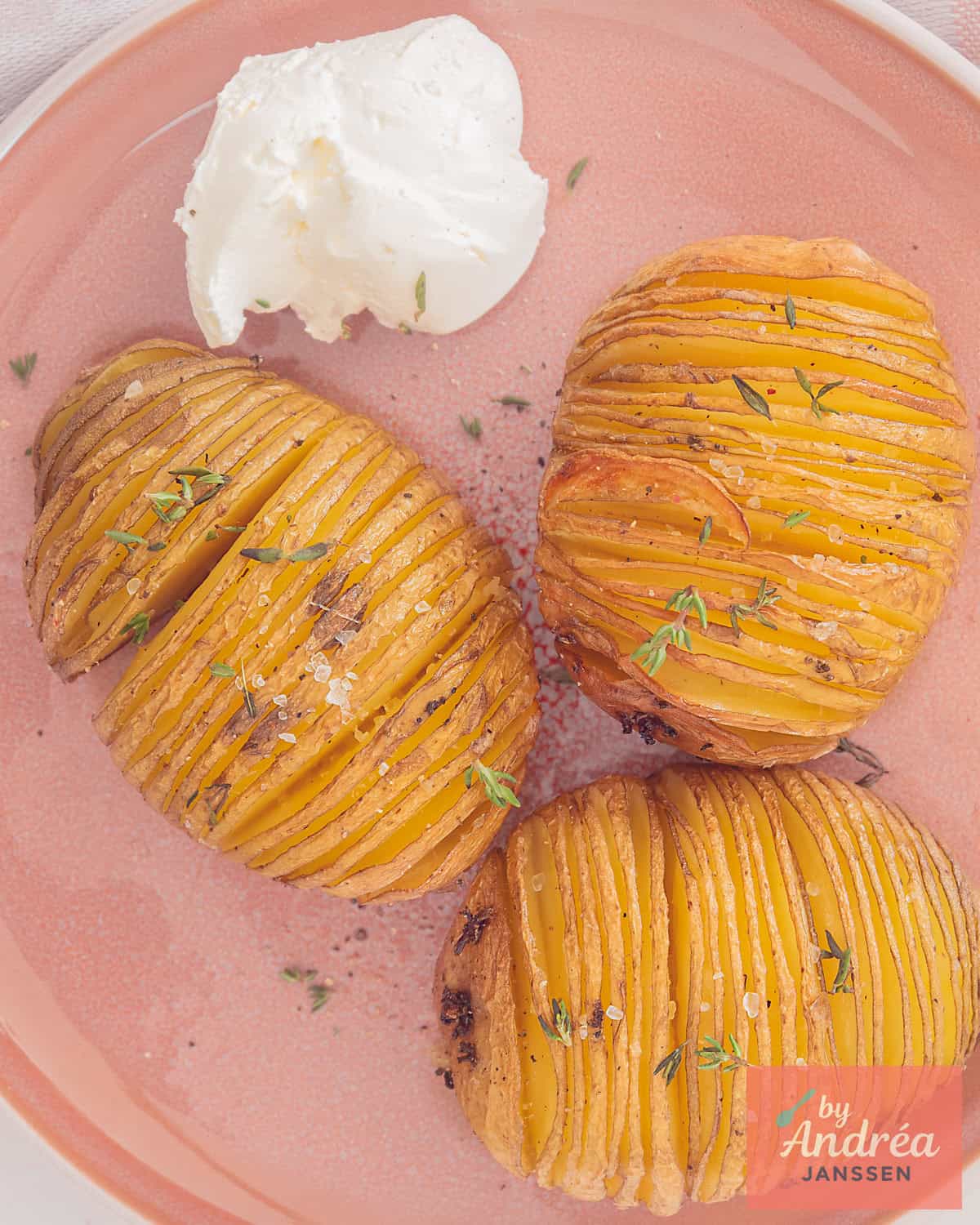 An overhead shot of a pink plate with three hasselback potatoes and some sauce.