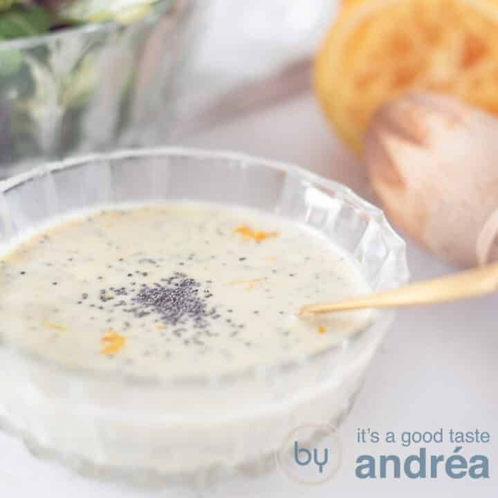 A square photo with a bowl of Honey Mustard dressing with orange zest and poppy seeds. A white background. Top right a squeezed orange. Top left a green salad