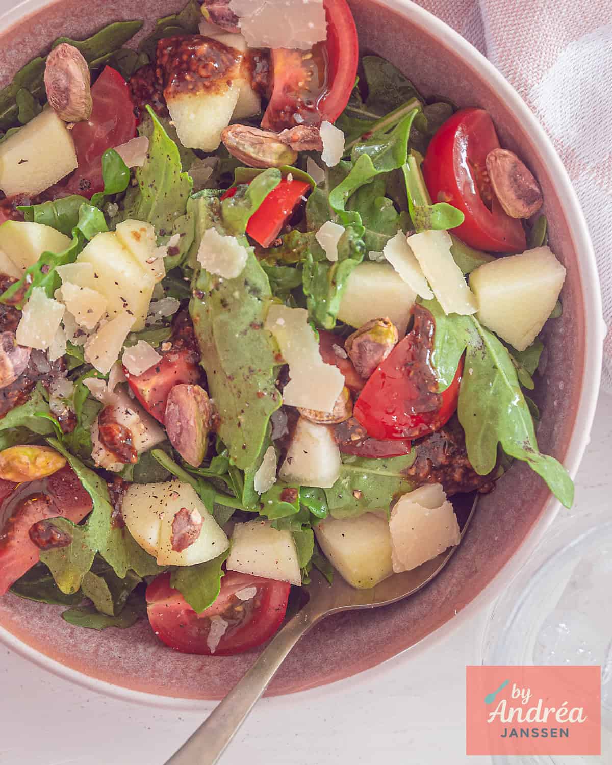An overhead photo of an arugula salad with pistachios, apple, pear, and tomatoes.