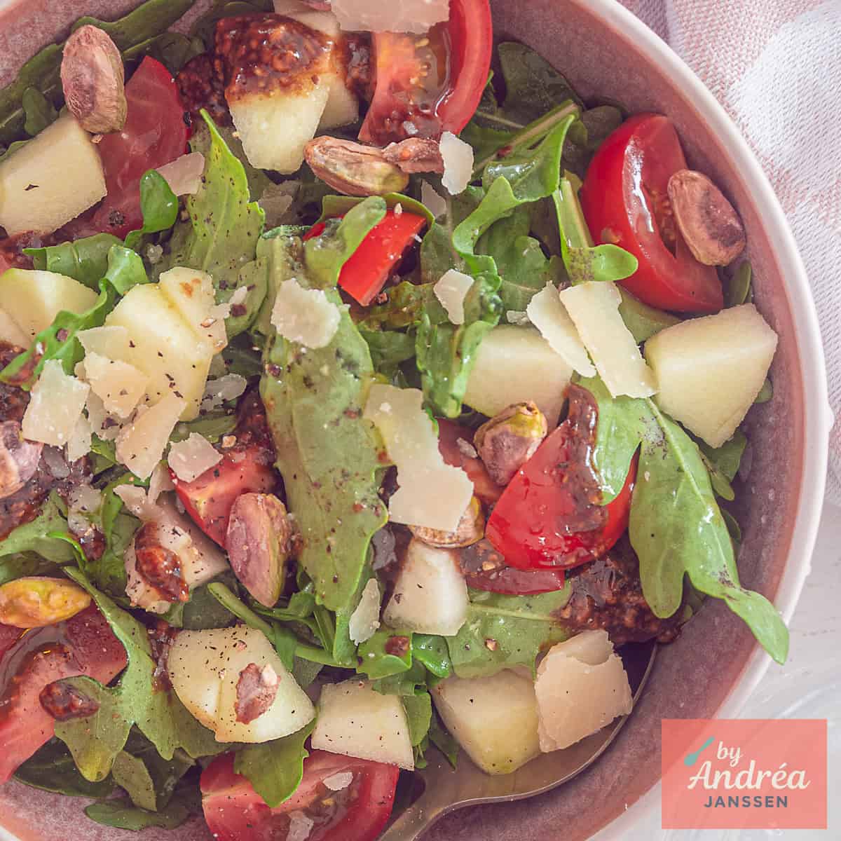 A square photo from above of a salad of arugula, tomato, pear, apple and pistachios