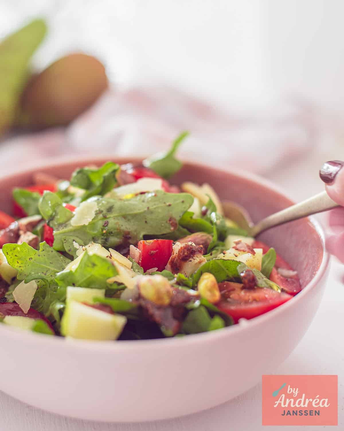 A pink bowl with a rocket salad with tomatoes, apple, pear and pistachios