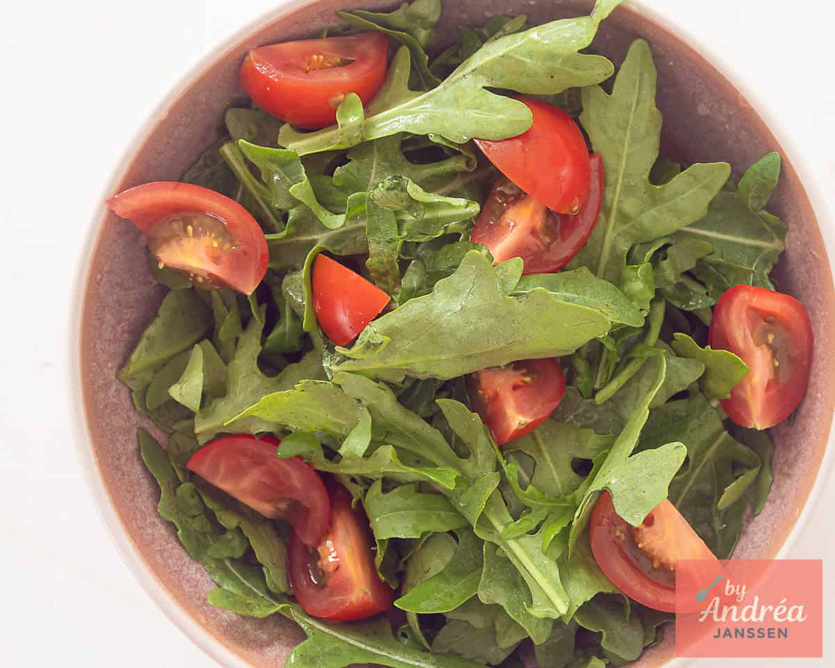 A pink bowl with arugula and quartered tomatoes