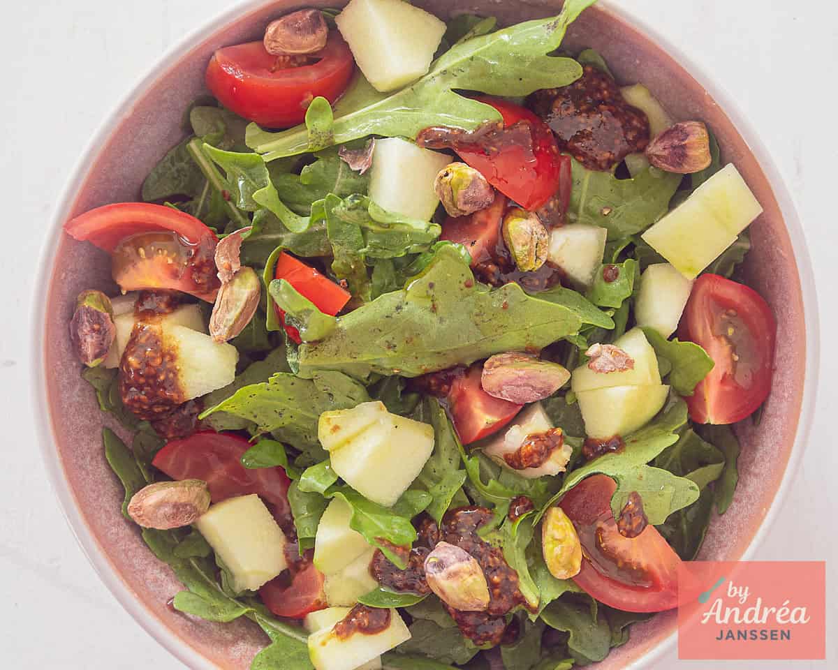 A salad with apple, pear, pistachio and tomatoes in a pink bowl