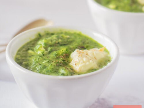 A square photo of two bowls of arugula spinach soup with creme fraiche.