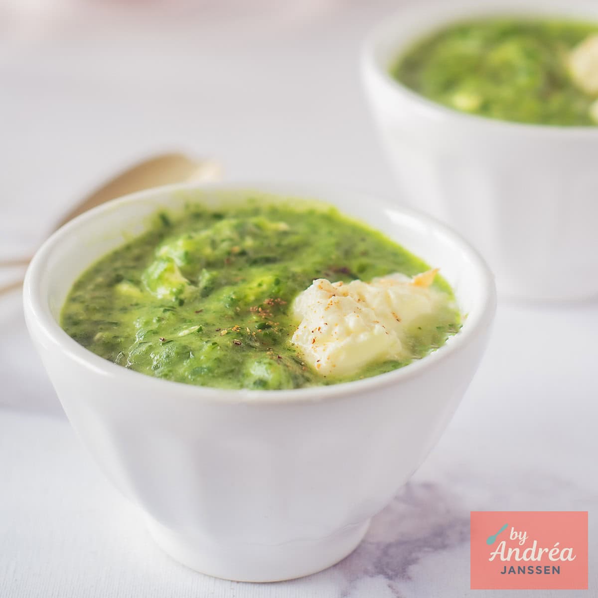 A square photo of two bowls of arugula spinach soup with creme fraiche.