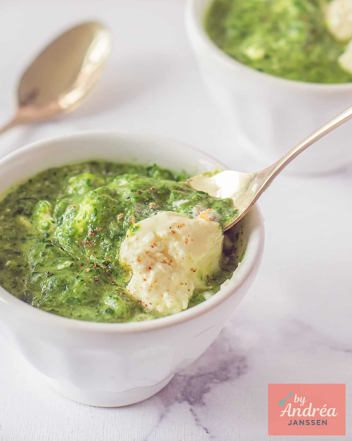 A bowl of soup with arugula, spinach, and potatoes. A spoon takes a scoop
